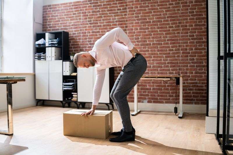 Man In Office Lifting Heavy Box With Back Pain